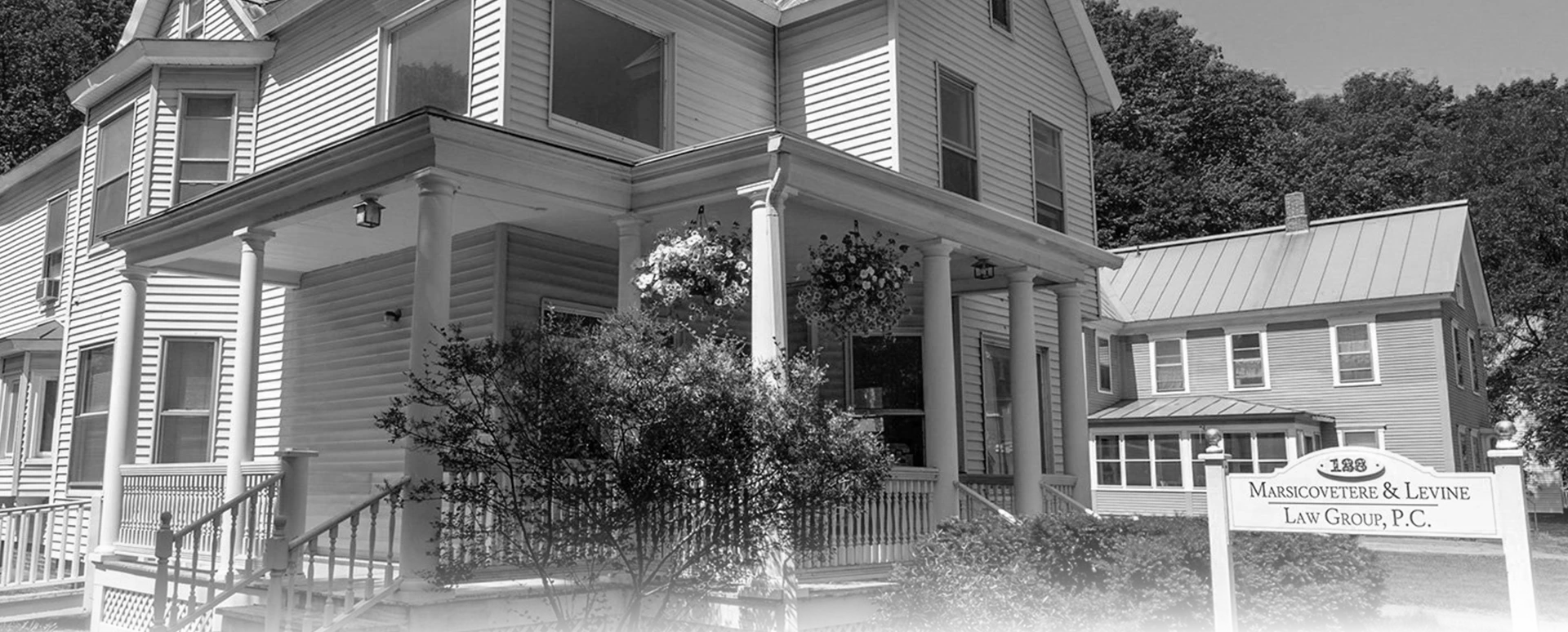 Black and white Marsicovetere & Levine Law Group office building with a porch, columns, and foliage.