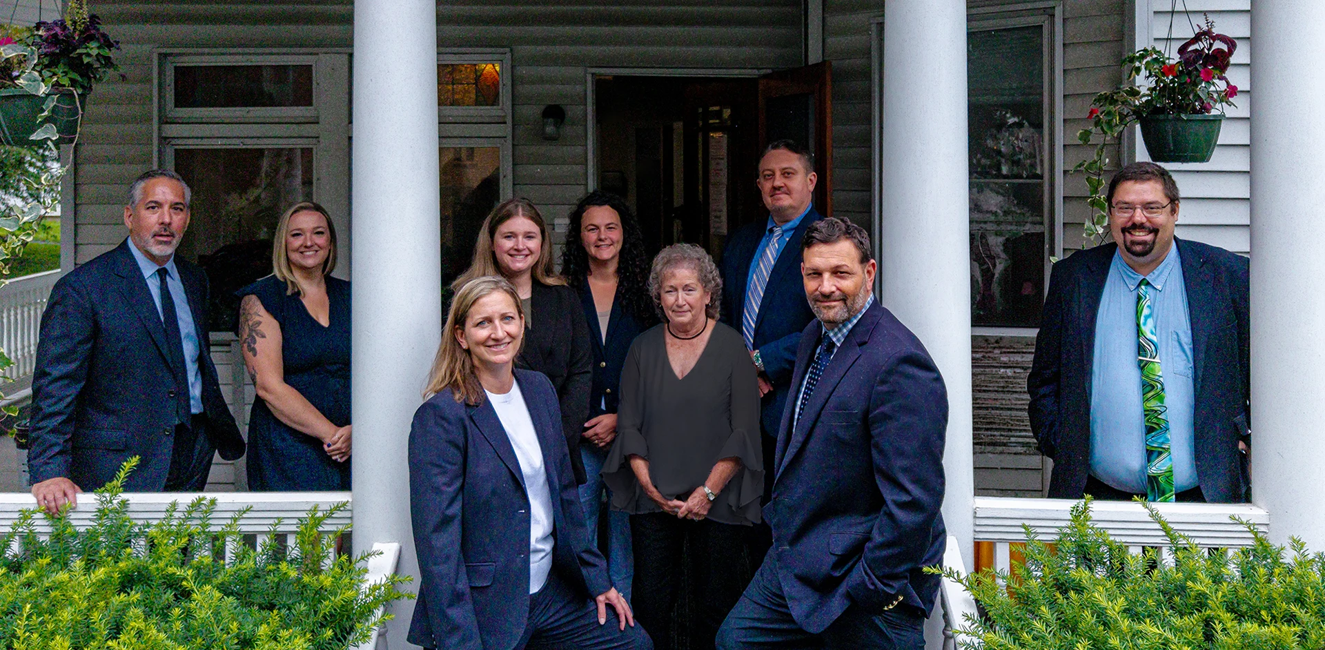 Marsicovetere & Levine Law Group team smiles while standing on a house porch with white pillars.